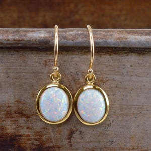 Könnte beinhalten: Ein Paar goldene ovale Ohrringe mit weißen Opal-Steinen.
