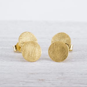 Könnte beinhalten: Ein Paar goldfarbene Ohrstecker mit strukturierter Oberfläche. Jeder Ohrstecker besteht aus zwei sich überlappenden Kreisen.