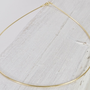 Op de afbeelding: Een dunne gouden kettingketting op een wit houten oppervlak.