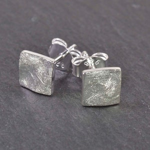 Peut inclure: Une paire de boucles d'oreilles clous carrées en argent avec une finition texturée.