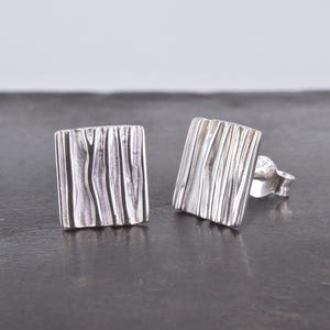 May include: A pair of silver square stud earrings with a textured, wood-like design.