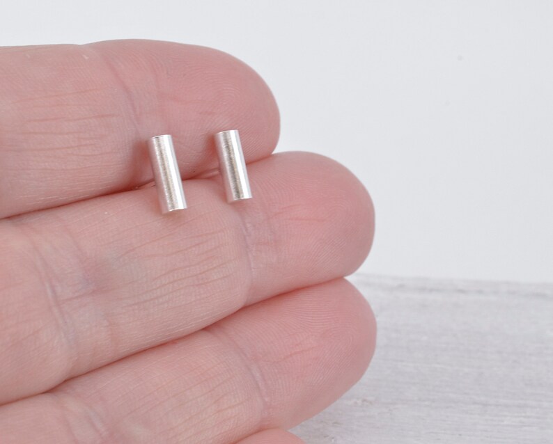 May include: A pair of silver bar stud earrings. The earrings are simple and minimalist, and they are perfect for everyday wear.