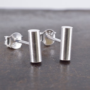 May include: A pair of silver bar stud earrings. The earrings are simple and minimalist, with a smooth, polished finish.