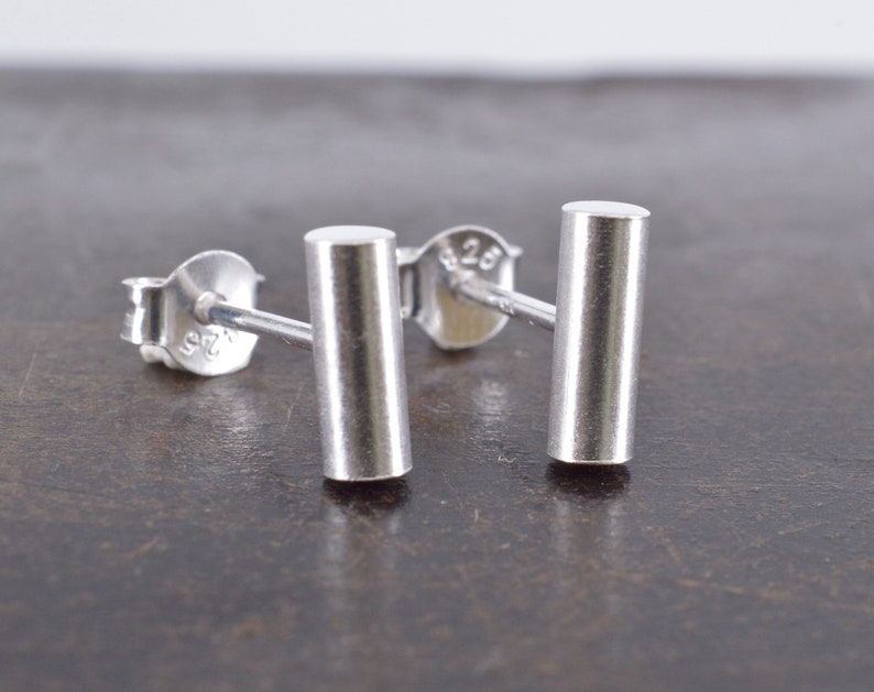 May include: A pair of silver bar stud earrings. The earrings are simple and minimalist, with a smooth, polished finish.