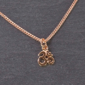 Könnte beinhalten: Eine Halskette aus Roségold mit einem kleinen Anhänger in Form eines Om-Symbols.