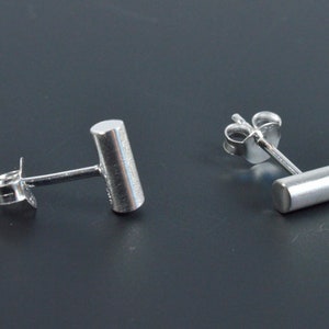 May include: A pair of silver stud earrings with a cylindrical design. The earrings are simple and minimalist.