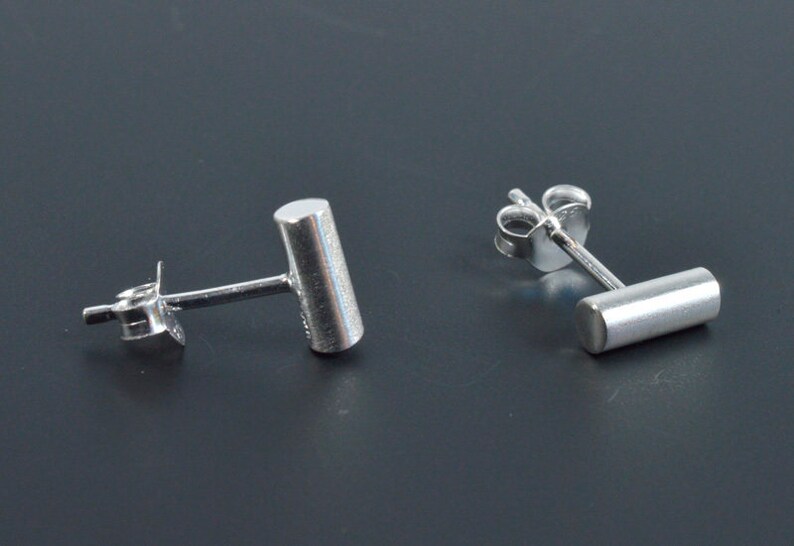 May include: A pair of silver stud earrings with a cylindrical design. The earrings are simple and minimalist.
