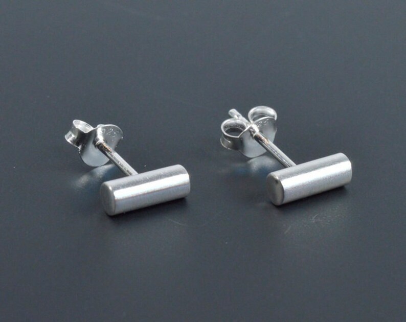 May include: A pair of silver stud earrings with a small, rectangular bar. The earrings have a simple, minimalist design.