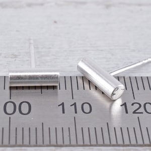 May include: Two silver bar earrings, one is laying flat on a ruler marked with inches, the other is standing upright. The ruler shows measurements from 100 to 120.