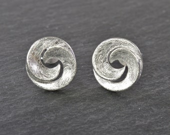 May include: A pair of silver earrings with a swirling, textured design. The earrings are circular and have a slightly raised edge.