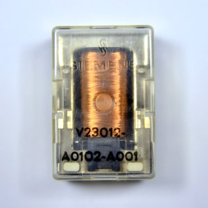 May include: A clear plastic box containing a copper-colored coil with the text "SIEMENS" and "V23012-A0102-A0013" printed on it.