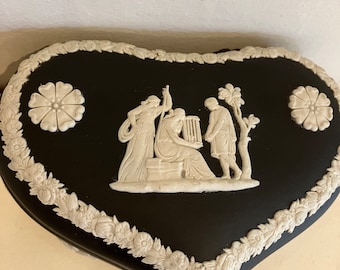 May include: Black heart-shaped trinket box with a white cameo design of three figures in a classical setting. The box is decorated with a white floral border.