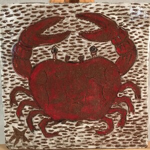 May include: A red ceramic tile featuring a hand-painted image of a crab. The crab is raised in relief and has a textured surface. The tile's background is white with brown dots.