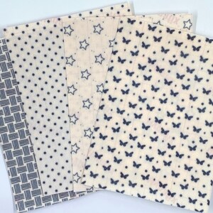 May include: A collection of reusable beeswax food wraps with various patterns. Designs include a blue and white woven pattern, polka dots, stars, and butterflies. The wraps are beige with blue designs, ideal for eco-friendly food storage.