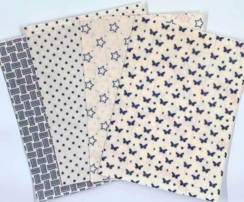 May include: A collection of reusable beeswax food wraps with various patterns. Designs include a blue and white woven pattern, polka dots, stars, and butterflies. The wraps are beige with blue designs, ideal for eco-friendly food storage.