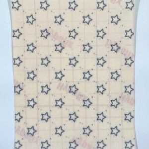 May include: A rectangular sheet with a repeating pattern of navy blue stars on a cream background. Small navy blue dots are interspersed between the stars. A grid pattern is faintly visible.