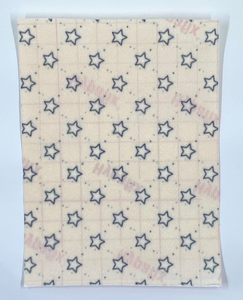 May include: A rectangular sheet with a repeating pattern of navy blue stars on a cream background. Small navy blue dots are interspersed between the stars. A grid pattern is faintly visible.