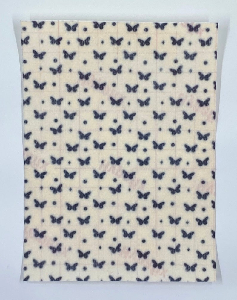 May include: A sheet of paper with a repeating pattern of dark blue butterflies and dots on a cream-colored background. The butterflies are evenly spaced in a grid-like arrangement. The paper is sealed in a clear plastic bag.
