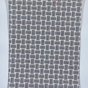 May include: A rectangular notebook with a woven pattern design. The pattern consists of navy blue horizontal and vertical lines on a cream-colored background. The notebook is encased in a clear plastic sleeve.
