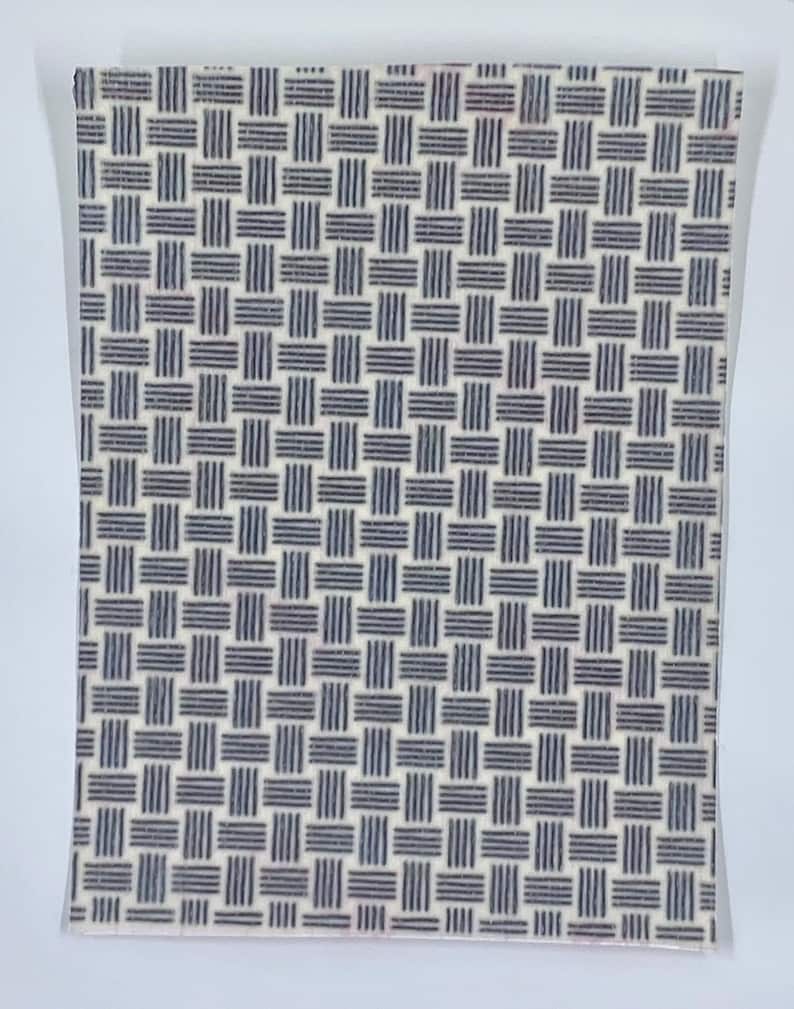 May include: A rectangular notebook with a woven pattern design. The pattern consists of navy blue horizontal and vertical lines on a cream-colored background. The notebook is encased in a clear plastic sleeve.