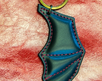 May include: A black leather keychain shaped like a bat wing with red stitching. The keychain has a brass key ring.