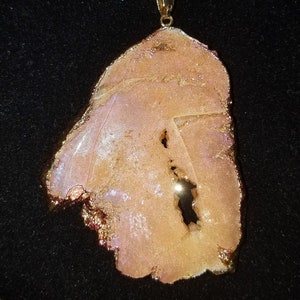 May include: A gold chain necklace with a large, irregularly shaped, pink and white agate pendant. The pendant has a natural, rough-hewn texture and a hole in the center.