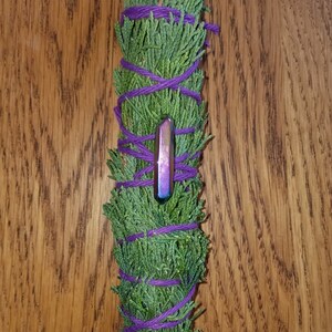 May include: A bundle of dried cedar leaves tied with purple string and a iridescent purple crystal point.