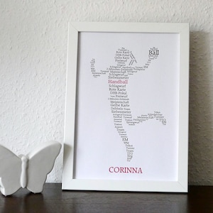 Könnte beinhalten: Ein gerahmter Druck mit einer Handballspieler-Silhouette, die aus Handballbegriffen in Schwarz besteht. Das Wort "Handball" ist rot. Der Name "Corinna" steht unten in Rot. Ein weißer Keramikschmetterling sitzt auf einer dunklen Oberfläche.