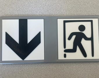 May include: A white sign with a black arrow pointing down and a black silhouette of a person running through a doorway. The sign is framed in gray.