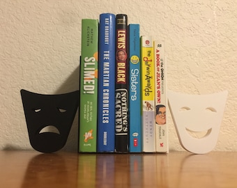 May include: A set of black and white bookends shaped like theater masks. The black mask is a sad face and the white mask is a happy face. The bookends are holding up a row of books with various titles.