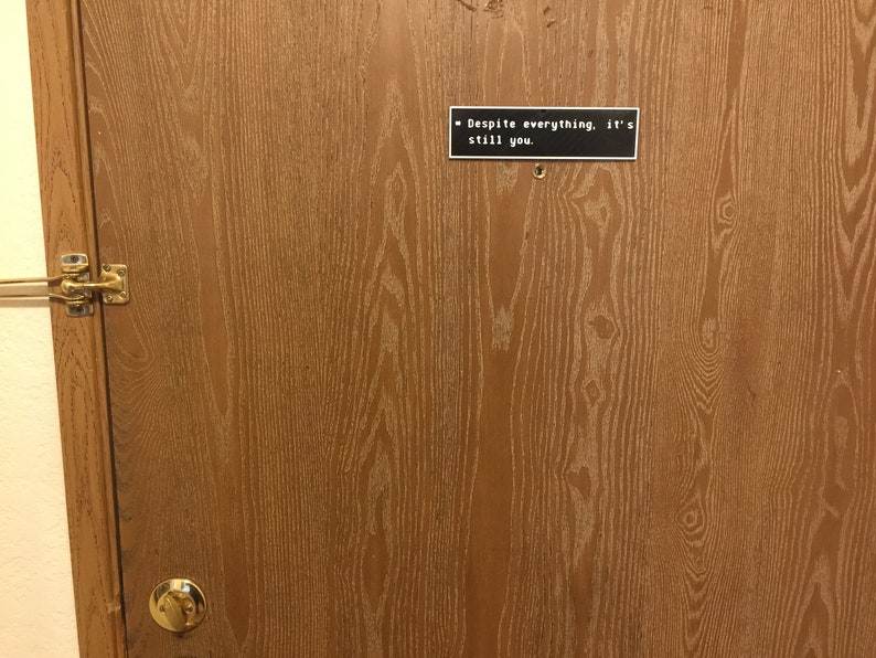 May include: A wooden door with a black sign that reads "Despite everything, it's still you."