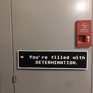 May include: A black and white sign with the text "You're filled with DETERMINATION." on a gray metal door with a red General Electric switch.