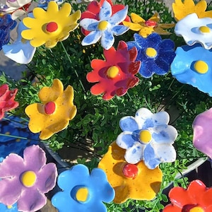 Könnte beinhalten: Ein Strauß bunter Keramikblumen mit gelben, roten, blauen, weißen und violetten Blütenblättern. Die Blumen sind in einer Vase arrangiert und haben grüne Stiele.