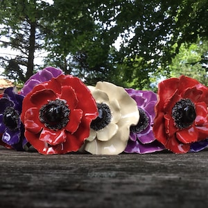 Könnte beinhalten: Eine Reihe von Keramikblumen in verschiedenen Farben, darunter Weiß, Rot, Lila und Schwarz. Die Blumen sind in einer Reihe auf einer Holzoberfläche angeordnet.