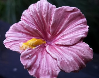 May include: A pink flower with a yellow center. The flower is made of ceramic and has a realistic appearance.