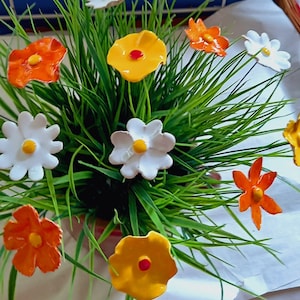 Könnte beinhalten: Ein Strauß Keramikblumen in einem grünen Gras-Pflanztopf. Die Blumen sind weiß, orange und gelb mit roten Zentren.