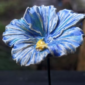 Pode incluir: Uma flor de cerâmica azul e branca com um centro amarelo. A flor está sobre um fundo preto.
