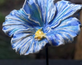 May include: A blue and white ceramic flower with a yellow center. The flower is on a black background.