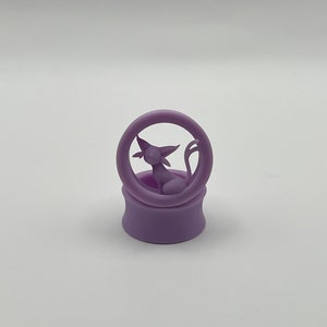 Może przedstawiać: Fioletowy silikonowy rozpylacz do uszu z wzorem kota. Kot siedzi w kółku.