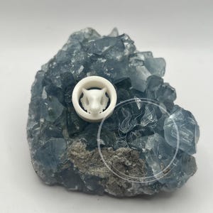 May include: White ceramic plug with a detailed animal face design, resting on a bed of blue crystals.
