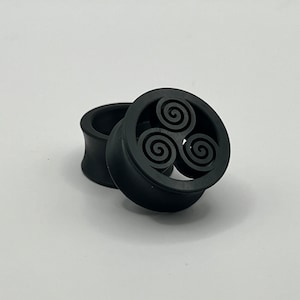 Könnte beinhalten: Ein Paar schwarze Silikon-Ohrenstrecker mit einem dreifachen Spiralendesign.