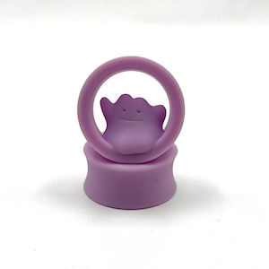 May include: Purple silicone ear gauges with a purple, cartoon-like ghost figure in the center.