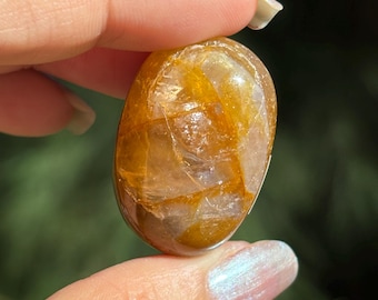 May include: A smooth, oval-shaped, golden citrine crystal with a translucent, cloudy appearance. The crystal has a natural, tumbled finish.