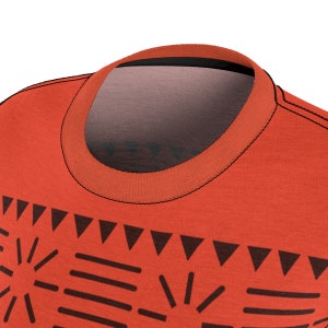 May include: A close-up of a red t-shirt with a black tribal pattern. The shirt has a crew neck and short sleeves.