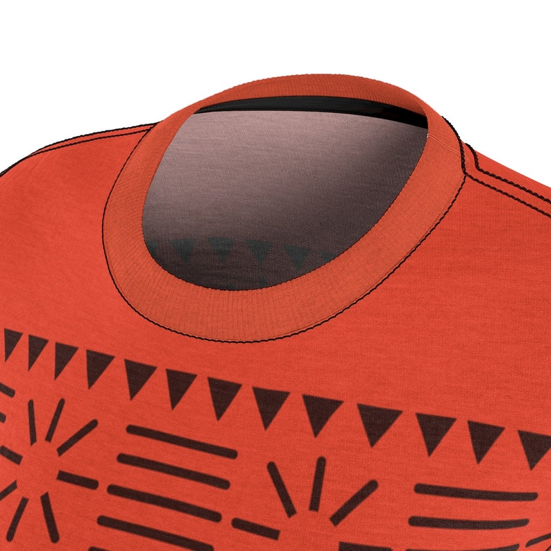 May include: A close-up of a red t-shirt with a black tribal pattern. The shirt has a crew neck and short sleeves.