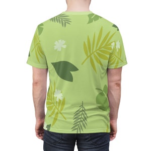 May include: A light green t-shirt with a tropical leaf pattern. The leaves are in shades of green and yellow. There are also white flowers on the shirt.