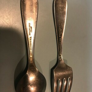 K&ouml;nnte beinhalten: Ein Vintage-Set aus L&ouml;ffel und Gabel aus Edelstahl. Der L&ouml;ffel hat eine abgerundete Sch&uuml;ssel, und die Gabel hat vier Zinken. Beide Utensilien tragen die Aufschrift "SEI HAMONO K.K. STAINLESS JAPAN" auf den Griffen. Das Set ist aus silberfarbenem Metall gefertigt.