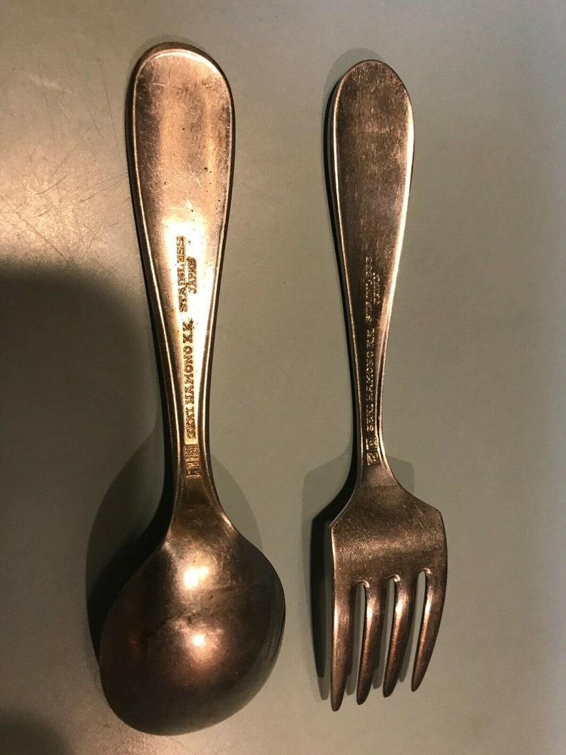 K&ouml;nnte beinhalten: Ein Vintage-Set aus L&ouml;ffel und Gabel aus Edelstahl. Der L&ouml;ffel hat eine abgerundete Sch&uuml;ssel, und die Gabel hat vier Zinken. Beide Utensilien tragen die Aufschrift "SEI HAMONO K.K. STAINLESS JAPAN" auf den Griffen. Das Set ist aus silberfarbenem Metall gefertigt.