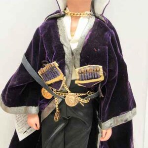 May include: A purple velvet robe with gold trim and a gold chain necklace. The robe has a decorative design on the front and is worn over a white shirt and black pants.