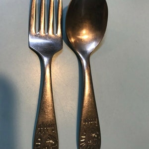 K&ouml;nnte beinhalten: Ein Vintage-Set aus Gabel und L&ouml;ffel aus Silber. Die Gabel hat vier Zinken und der L&ouml;ffel hat eine abgerundete Sch&uuml;ssel. Beide Utensilien haben ein dekoratives Design am Griff mit dem Wort "Rudolph" und einem Widderkopf.